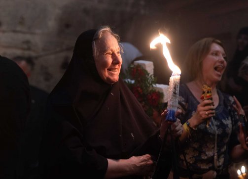 A smiling woman holds a torch during Sabt al-Nur observances in the Church of the Holy Sepulchre, April 4, 2023.