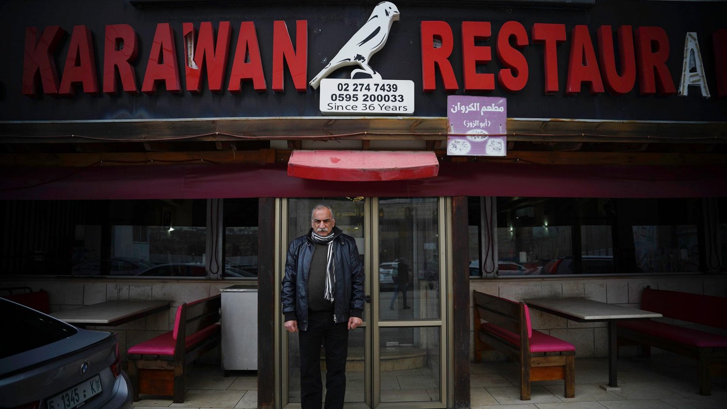 Abu Alzoz Nassar, owner of al-Karawan Restaurant, stands at its front door, which faces the Separation Wall, 2021.