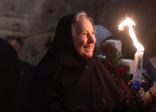 A worshipper smiles holding a candle lit during the Holy Fire ceremony in the Church of the Holy Sepulchre, 2023