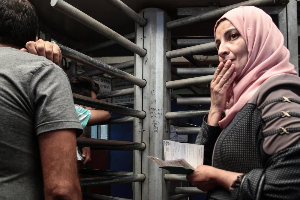 Woman holds her identity papers as she queues at Qalandiya checkpoint, 2016