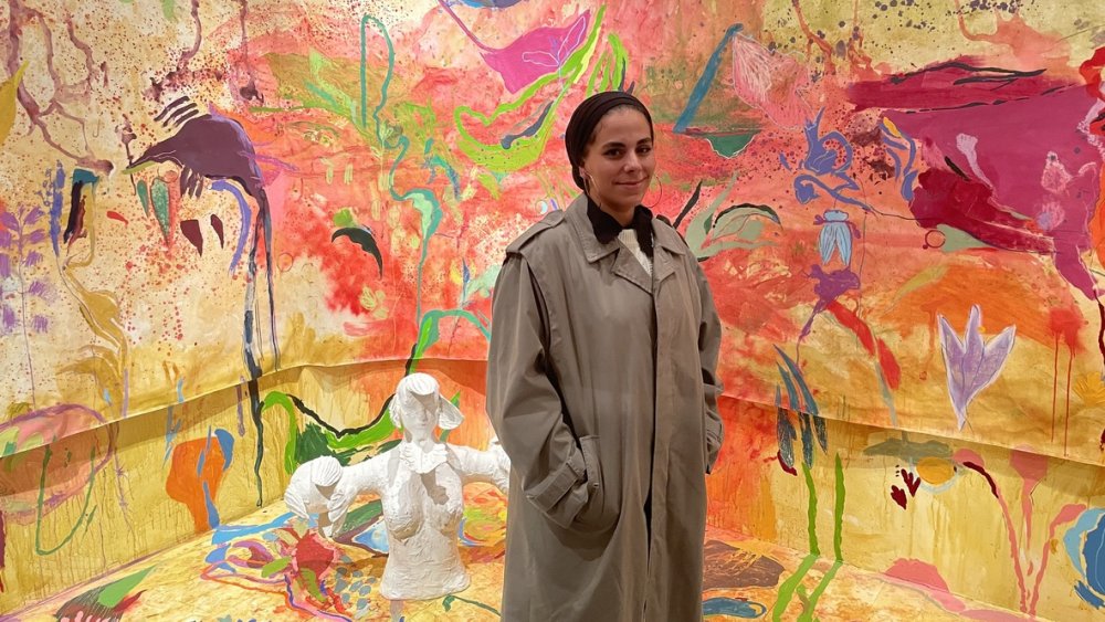 Sabreen al-Haj Ahmad stands in front of her painting, “Jerusalem Loose Orchids,” at al-Hoash's visual arts exhibition
