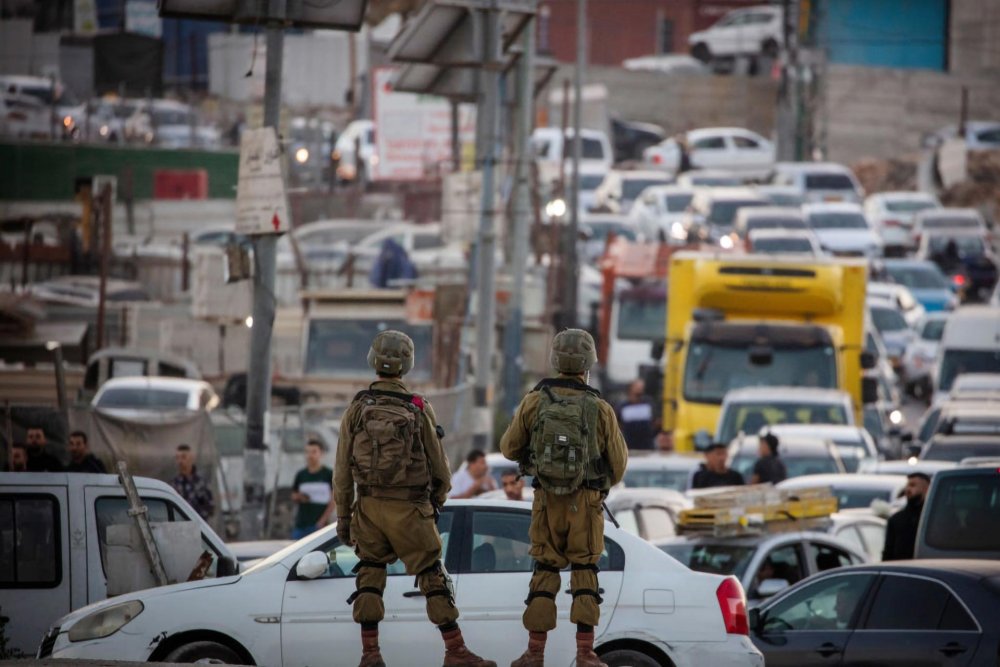 Two Israeli soldiers stand overlooking traffic trying to exit the Shu'fat refugee camp at its closed main artery.