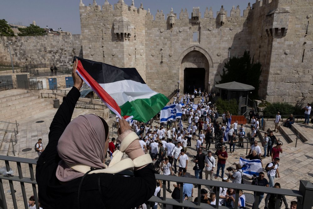 Israeli Flag Day marchers look up at a Palestinian woman flying a Palestinian flag from a balcony, 2022.