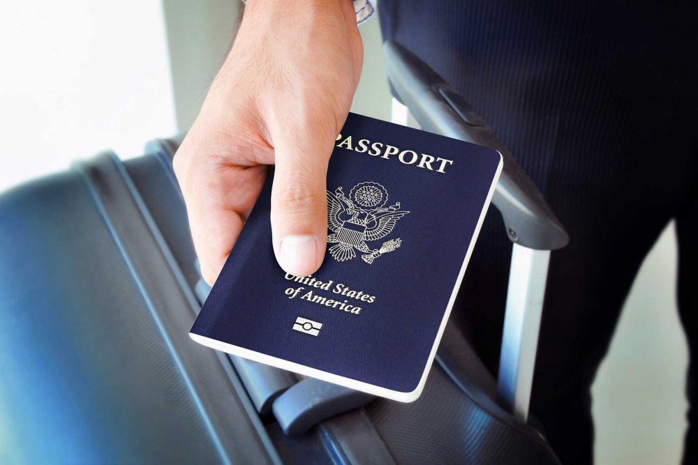Hand holding blue US passport with chip and suitcase