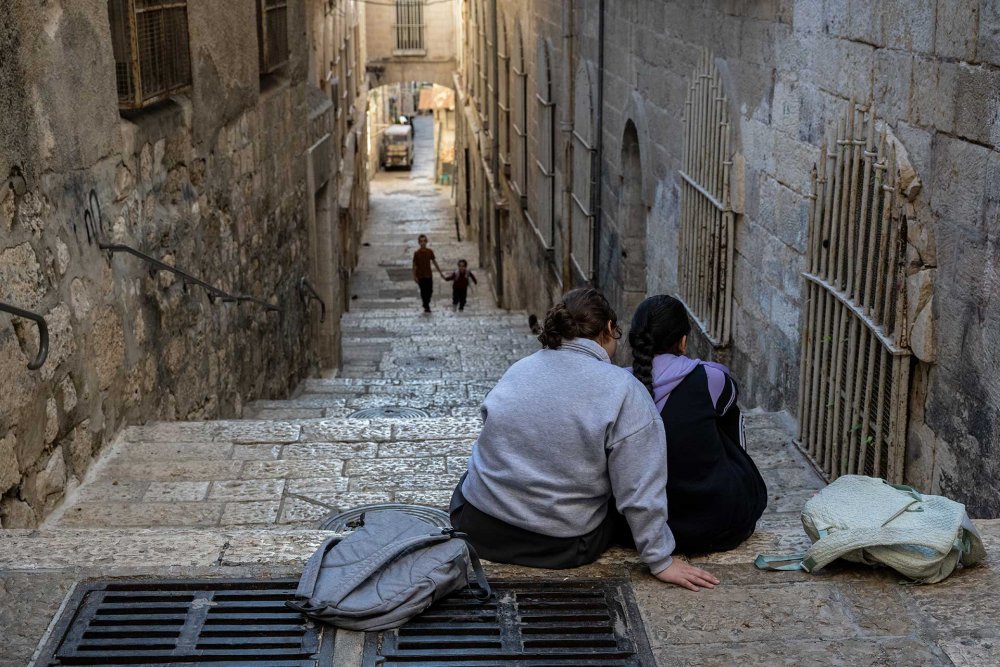 Two Palestinian schoolgirls sit on an alleyway step in the Old City, December 2, 2023.