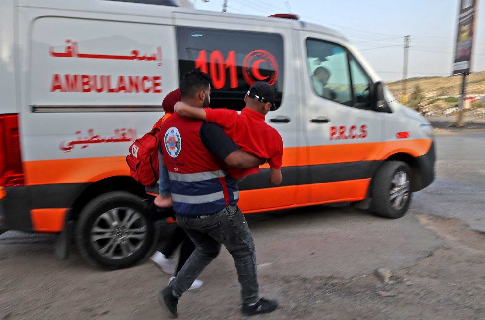 A Palestinian paramedic carries an injured patient to a waiting ambulance.
