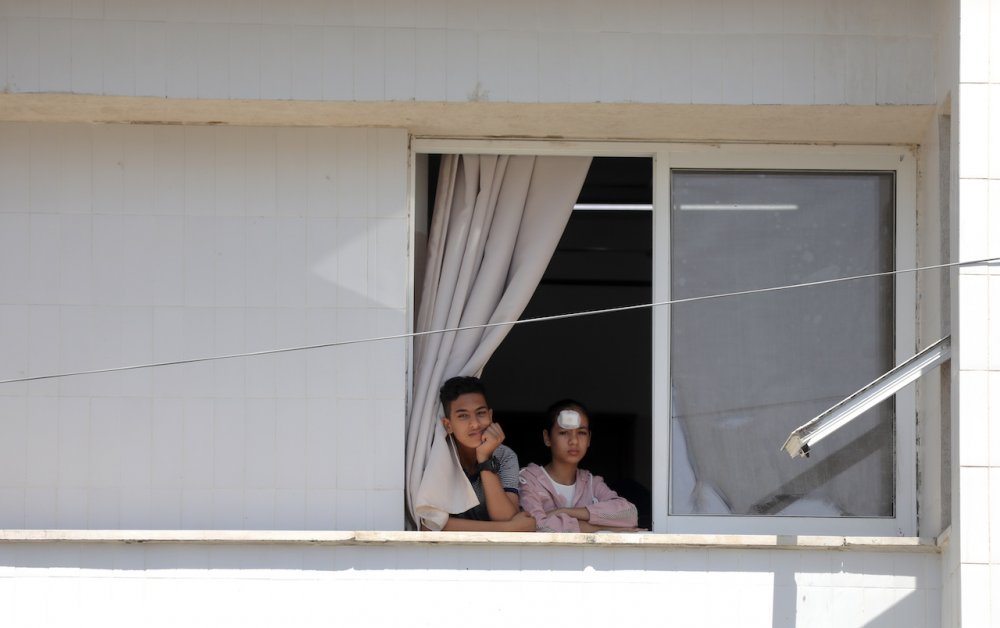 Young Palestinian brother and sister look woefully out a house window in Gaza City, August 16, 2022.