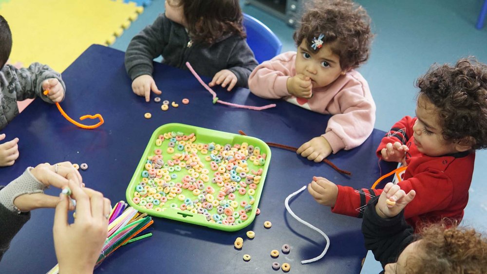 Toddlers learn to string fruit loops into necklaces at the YWCA, East Jerusalem, March 2024