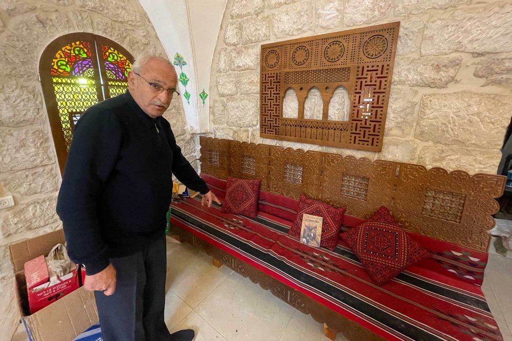 Azzam Abu Saud stands in front of a wooden couch at his art studio in Ras al-Amud, East Jerusalem, March 21, 2024.