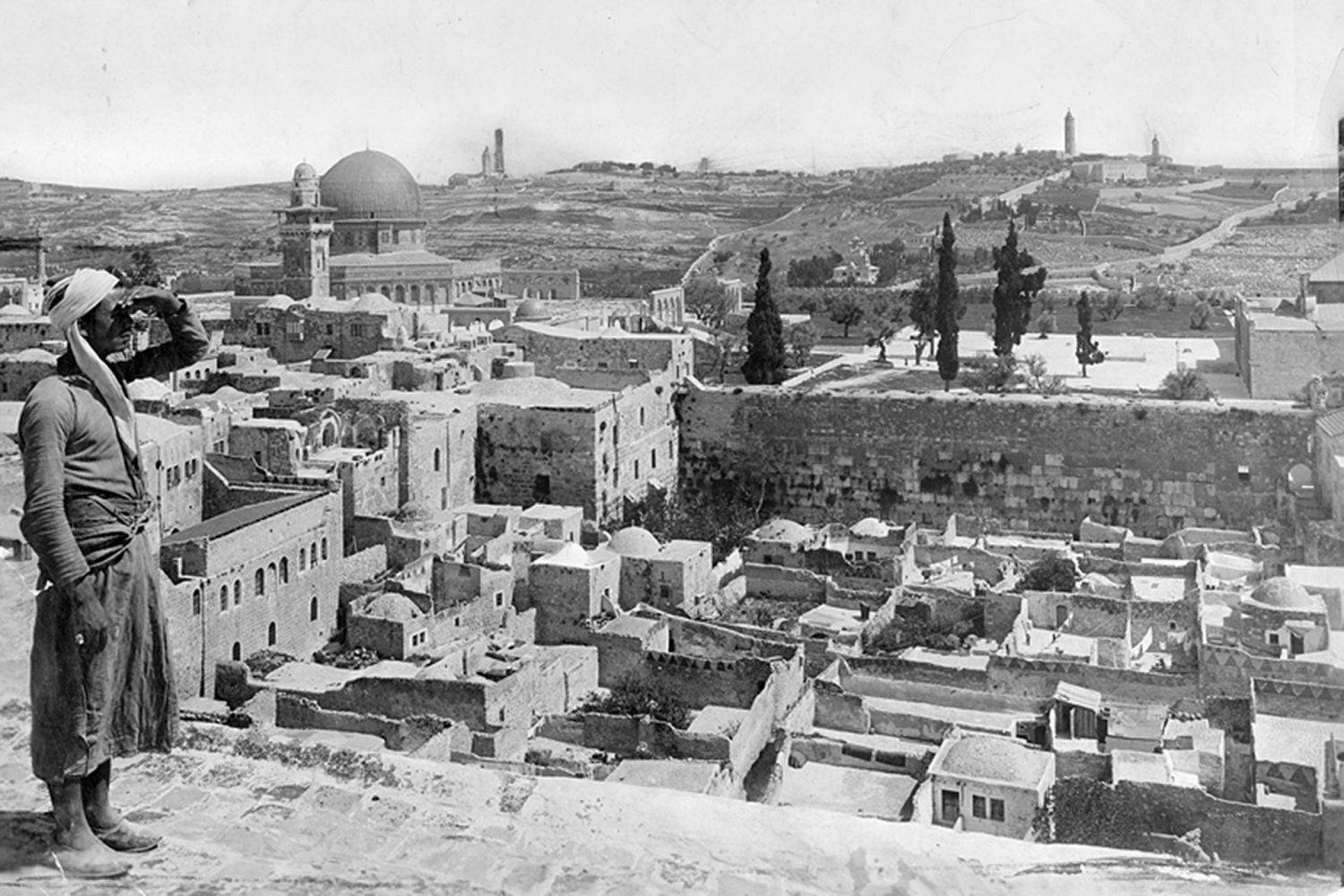 A man stands on a rooftop overlooking the Moroccan Quarter, with the Western (al-Buraq) Wall visible, 1917