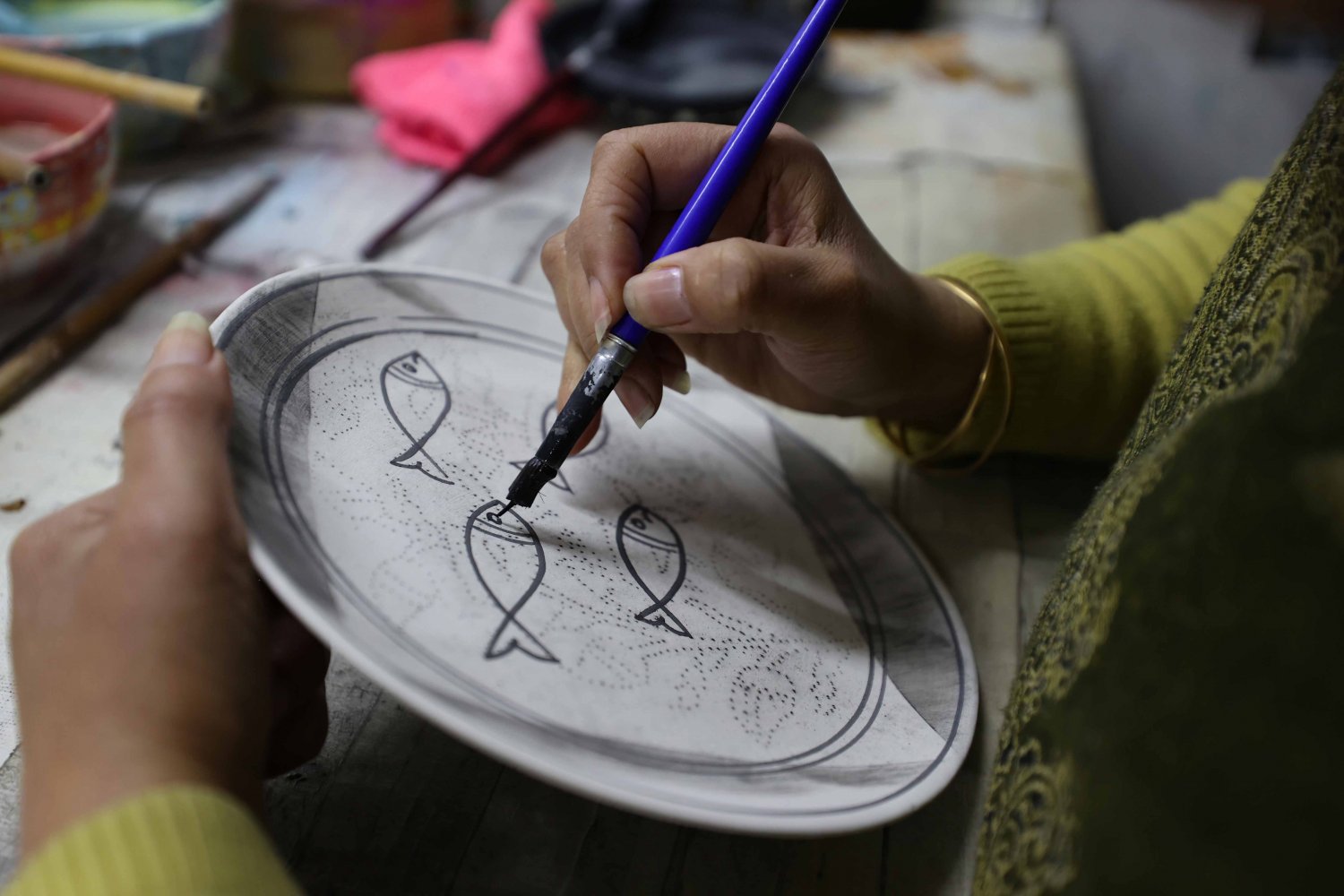 Ceramic artist Tahani al-Za‘ani outlines a fish design on an Armenian pottery plate at the Balian design studio 