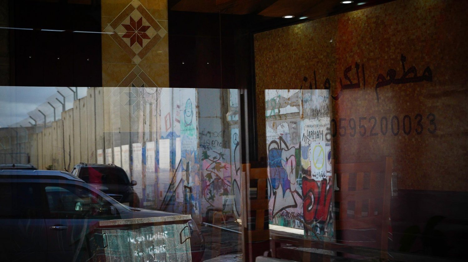 Israel's Separation Wall is reflected in the window of al-Karawan restaurant in Bethlehem, 2021