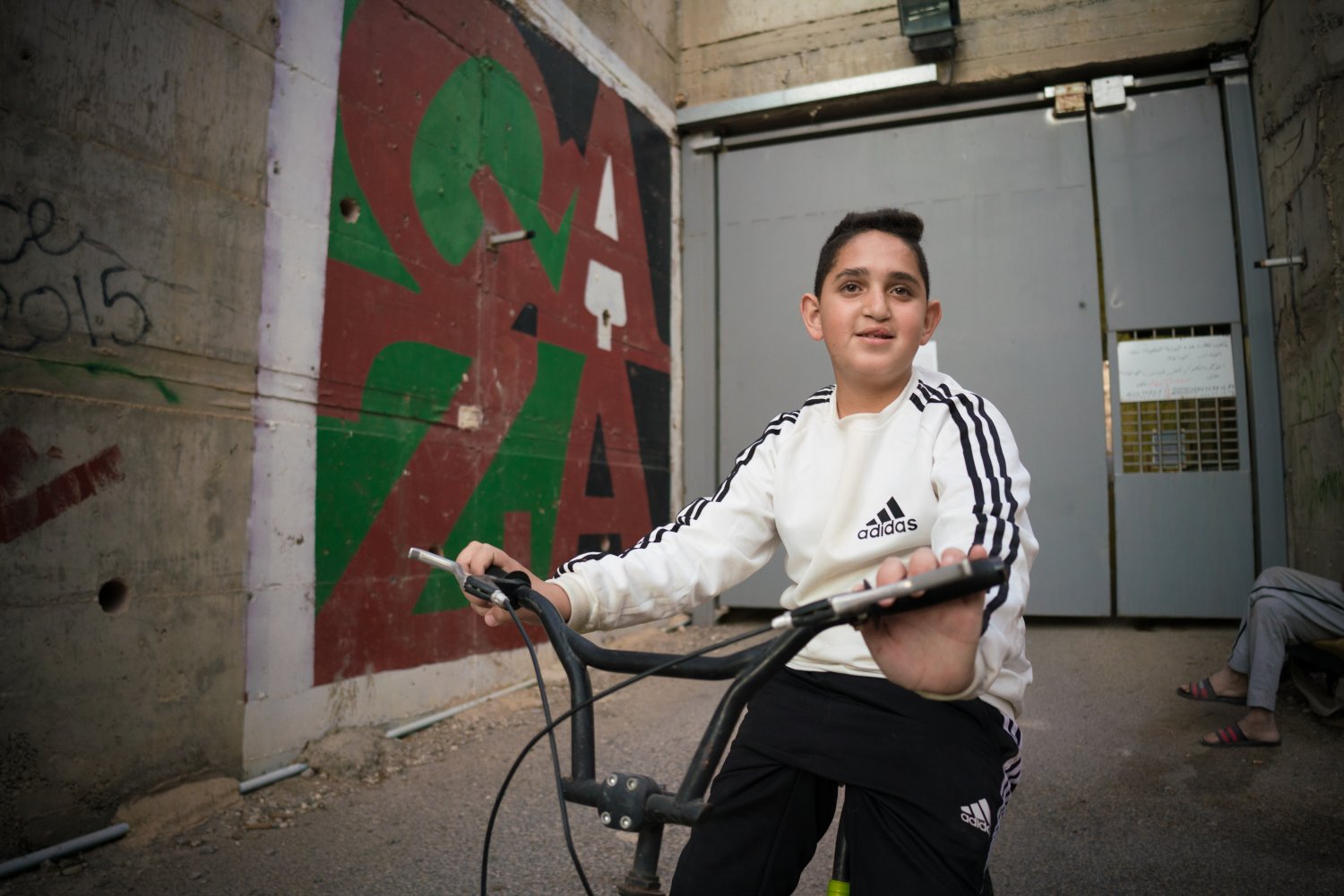Omar Hajajla’s youngest son bikes in front of the closed gate leading to their ghettoized home, 2021