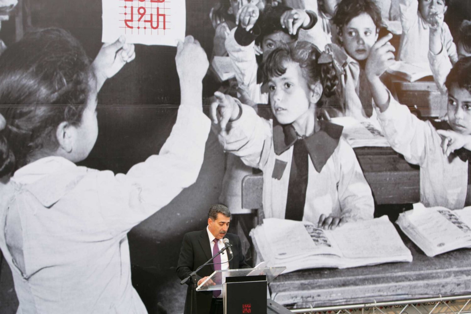 Ramallah Mayor Musa Hadid delivers the opening speech at Qalandiya International 2014 against a poster in the background designed by Jack Persekian