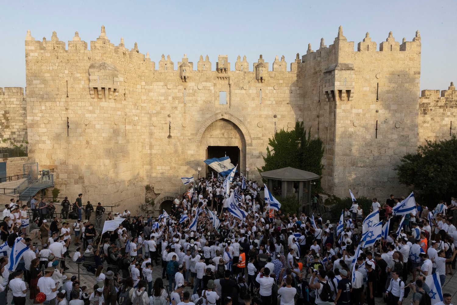 Israelis carrying blue-and-white Israeli flags march through Damascus Gate, Jerusalem’s main artery for Palestinians in the city.
