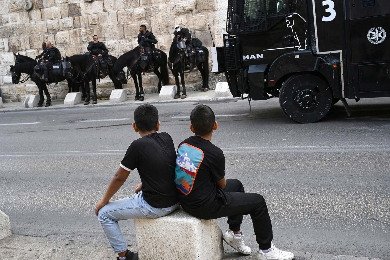 Two Palestinian children looking at Israeli soldiers on horses 