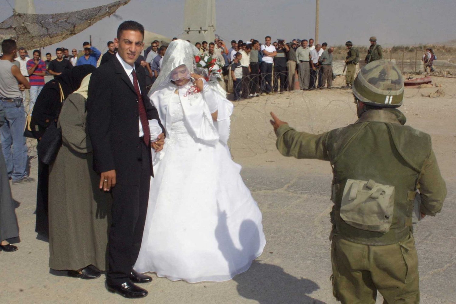 A bride and groom from Ramallah wait for an Israeli soldier to allow them to pass the Qalandiya checkpoint to Jerusalem to get married, September 23, 2002.